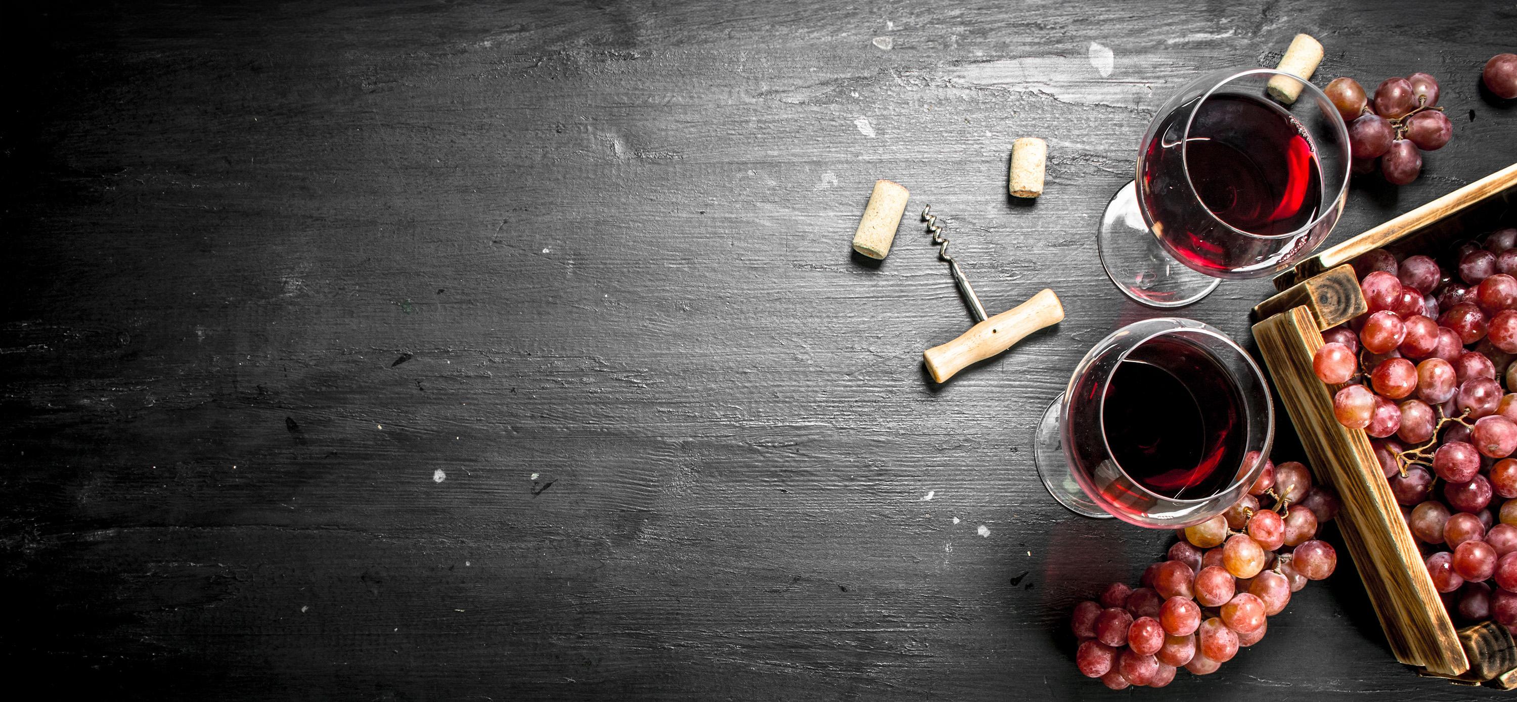 A cork screw, wine glasses, and grapes on a table.